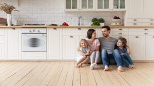 Happy Young Family With Little Children Sit On Warm Wooden Floor in New Modern Design Kitchen